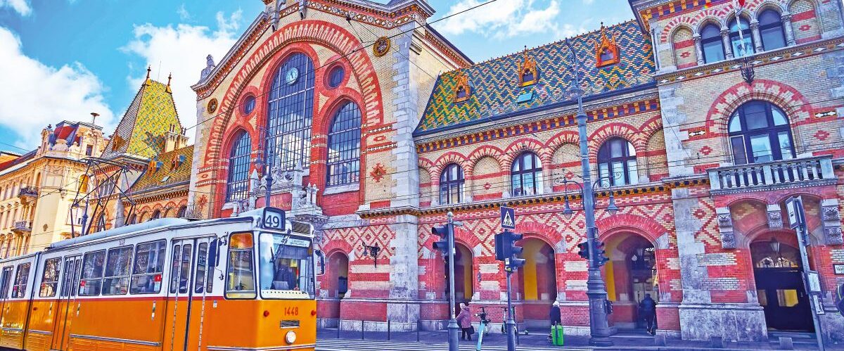 Vintage yellow tram, riding in front of the facade of Central Market Hall on Fovam Square, Pest, Budapest, Hungary